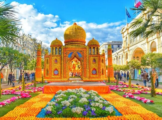 Vibrant lemon display of Taj Mahal replica with citrus fruits in a sunny garden setting, surrounded by colorful flowerbeds and palm trees.