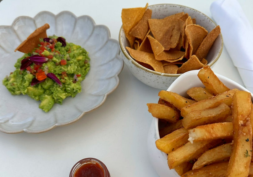 Guacamole with tortilla chips, fries, and sauce at Nikki Beach Monte Carlo. The guacamole is garnished with red and purple flowers.