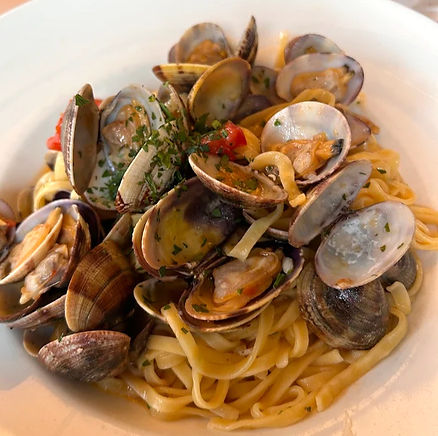 Close-up of linguine with clams, garnished with parsley and diced red peppers on a white plate. The dish appears fresh and appetizing.
