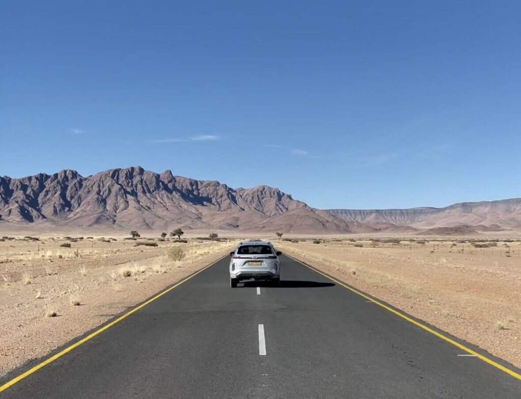 car in the middle of road in dessert with mountains