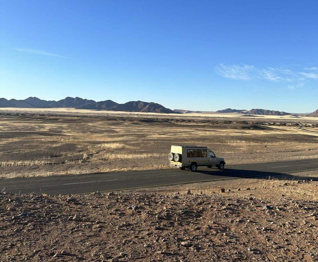 4x4 camper van driving on lonely road in the middle of african namibian desert with rocky mountain views