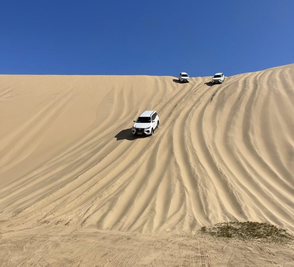 three 4x4 trucks driving down a tall dune in sandwhich harbour namibia